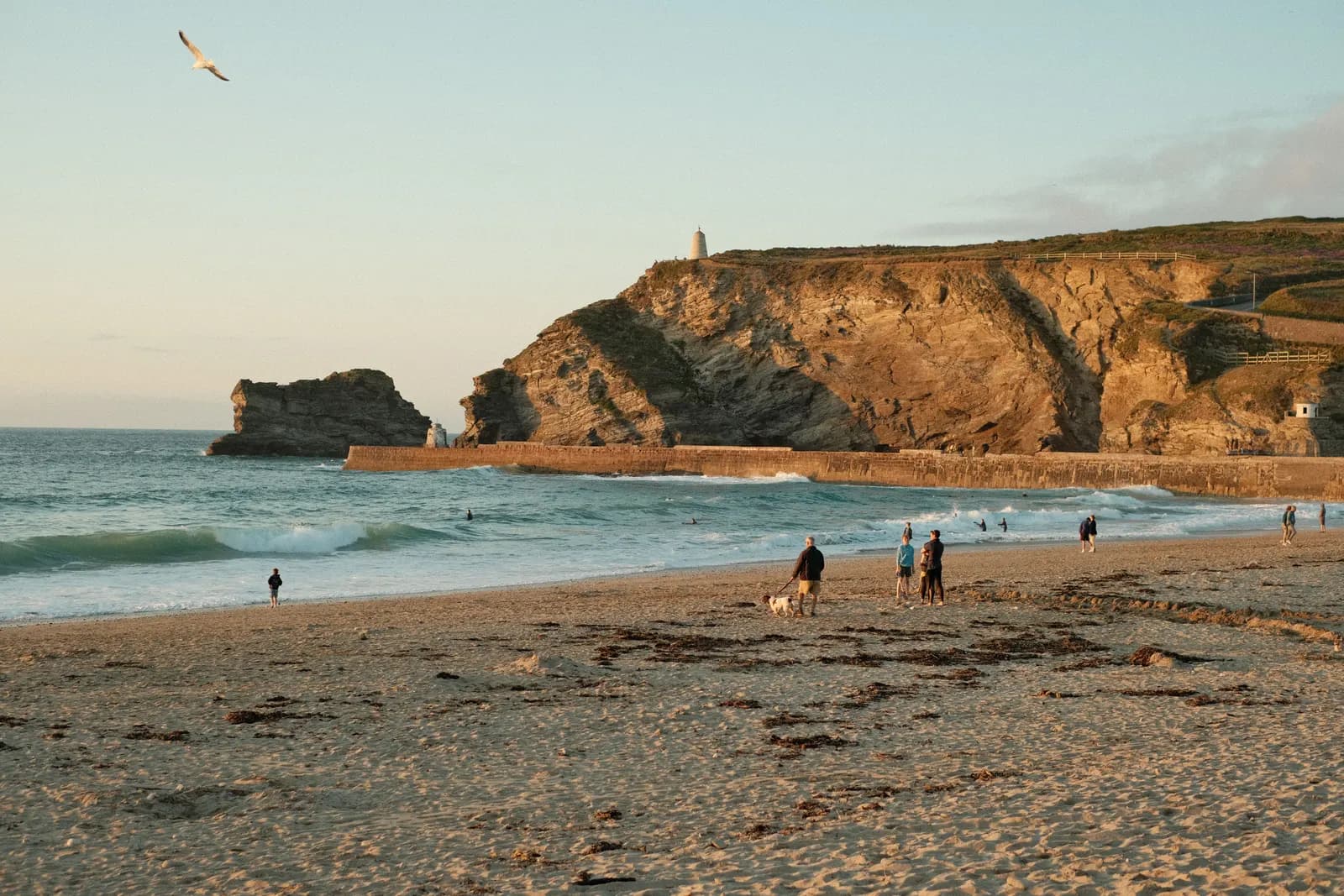 Families and a dog on the beach at Portreath, Cornwall, at golden hour with the harbour wall and cliffs behind