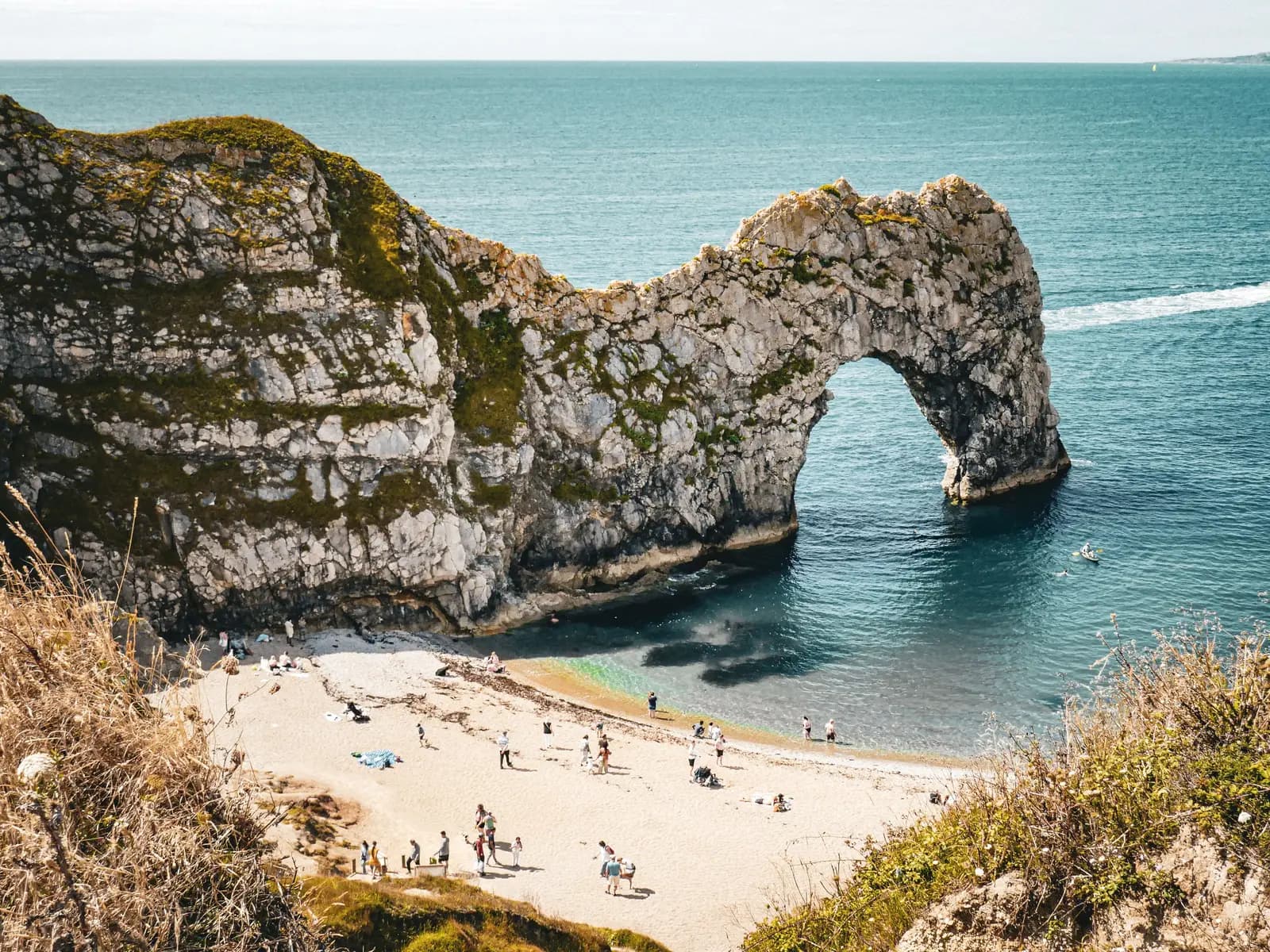 Visitors on the beach beneath a limestone sea arch on the Dorset coast, with the arch framing the water beyond