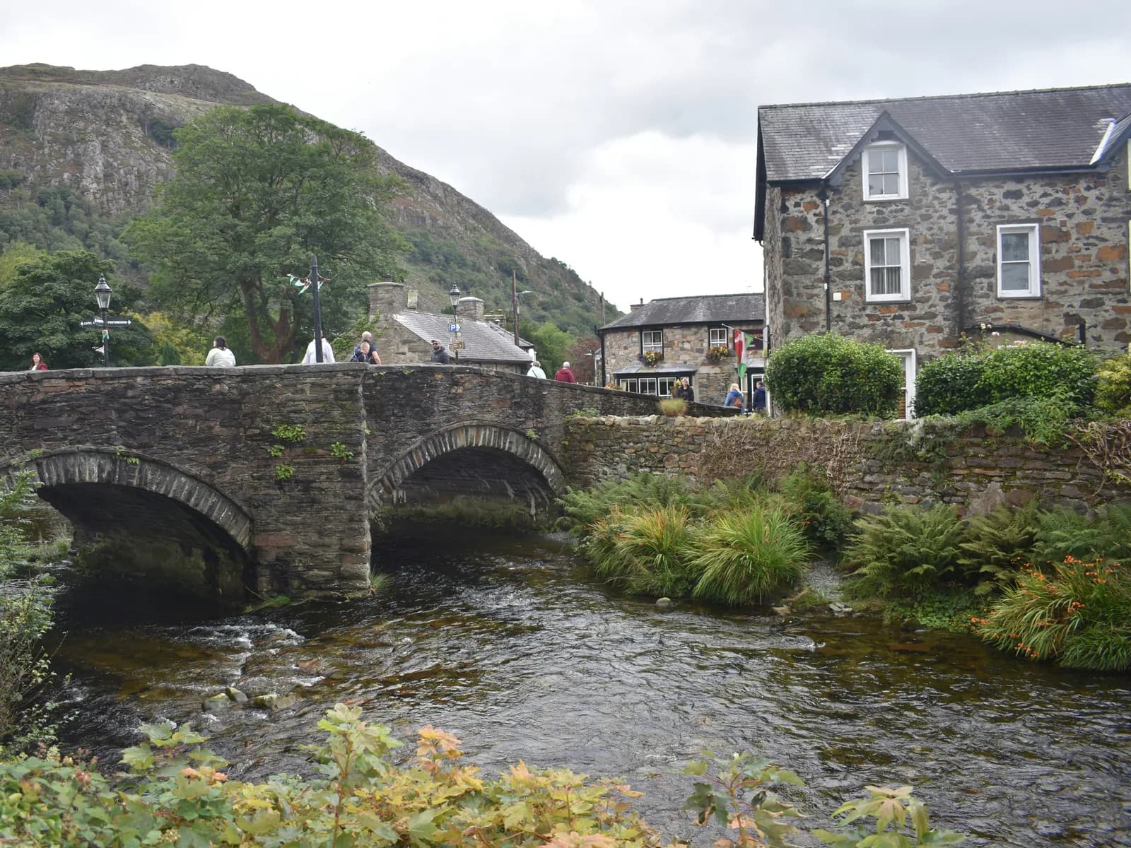 A stone packhorse bridge over a river in a Snowdonia village, with stone cottages and hills beyond